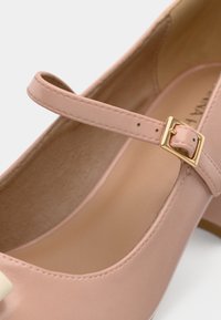 Pantof de tip Mary Jane din piele roz deschis, cu vârf rotund, o curea subțire peste laba piciorului și un accent cu cataramă auriu. Textură netedă, toc modest.