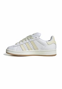 White leather sneaker with cream accents, featuring three side stripes, textured laces, and a rubber sole. Minimalist design with padded collar.