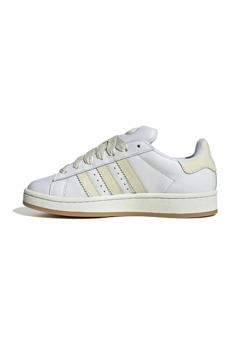 White leather sneaker with cream accents, featuring three side stripes, textured laces, and a rubber sole. Minimalist design with padded collar.
