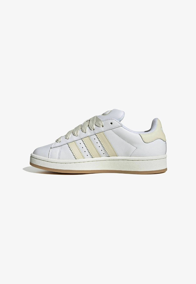 White leather sneaker with cream accents, featuring three side stripes, textured laces, and a rubber sole. Minimalist design with padded collar.