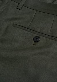 Olivgröna byxor i texturerat tyg, med en framficka och en svart knappdetalj. Klassisk design med strukturerade veck.