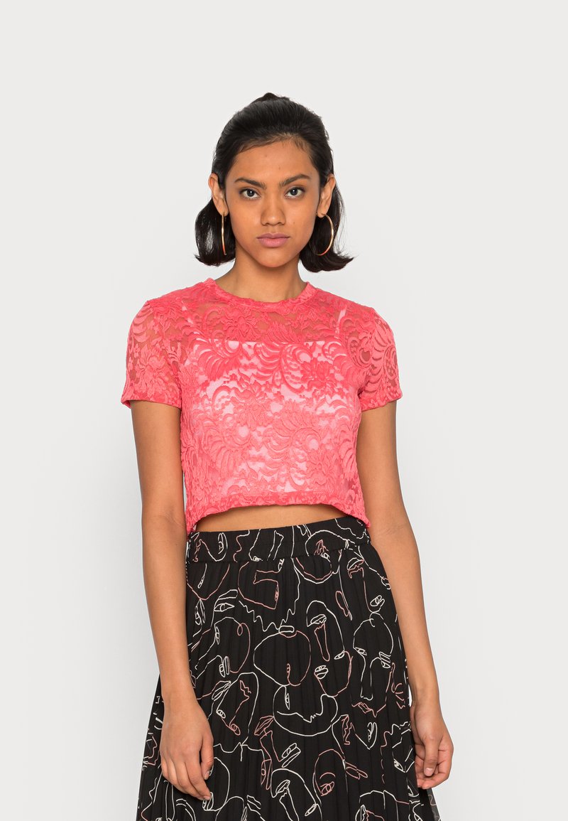 Top cropped em renda rosa com padrão floral, mangas curtas e decote redondo, combinado com uma saia preta com desenhos abstratos brancos.