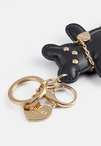 Llavero negro de cuero en forma de oso con herrajes en tono dorado, que cuenta con tres anillas circulares y un charm en forma de corazón con texto grabado.