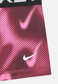 Nohavice Nike na aktívny život v gradientnom vzore s odtieňmi gaštanovej a ružovej, s bielym logom a textúrovaným materiálom.