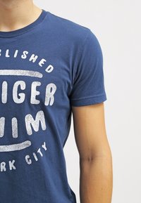 Námořnický modrý bavlněný tričko s bílým grafickým potiskem s textem "TIGER" a "NEW YORK CITY", krátké rukávy a kulatý výstřih.