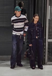 Camicia a maniche lunghe a righe, jeans blu, cappellino verde; giacca e pantaloni scuri con borchie; borsa nera con dettagli in pelliccia.