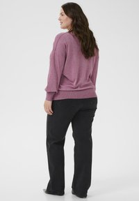 Rosa strukturierter Pullover mit überschnittenen Schultern, kombiniert mit schwarzen gerade geschnittenen Jeans mit Gesäßtaschen. Glattes Material und lockere Passform.