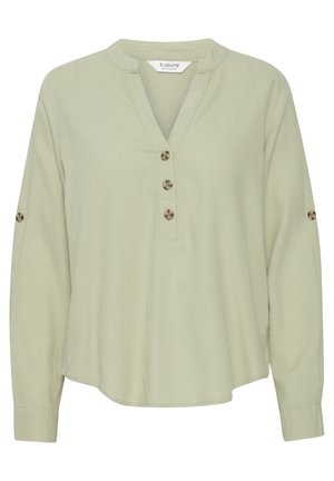 Bluză lungă cu mânecă lungă de culoare verde deschis, dintr-un material moale, cu un placket cu nasturi și tiv rotund. Prezintă două nasturi pe fiecare mânecă pentru detaliu.