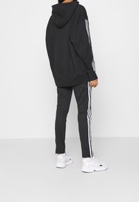 Black oversized hoodie with a hood, paired with black joggers featuring white side stripes and white athletic sneakers.