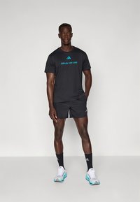 Sort atletik t-shirt med teksten "FØLG LINJEN" i blåt, kombineret med sorte shorts, sorte sokker og lyseblå og hvide løbesko.