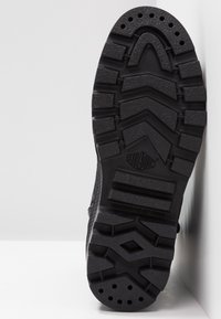 Černá podrážka boty s hlubokým vzorem, včetně obdélníkových a chevronových tvarů, se značkou "Palladium" a textem "Navrženo pro městský terén".