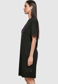 Czarna, oversize sukienka t-shirt wykonana z bawełny, z krótkimi rękawami, z graficznym nadrukiem z przodu. Dół kończy się tuż nad kolanem.