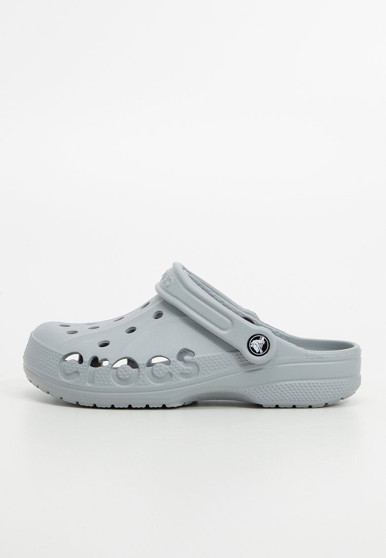 Zueco de color gris claro, tipo slip-on, con agujeros de ventilación, correa ajustable en el talón, suela texturizada y nombre de la marca embossado en el lateral.