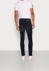 Jeans de mezclilla negra con un corte ajustado, detalles de costura sutil y dos bolsillos traseros. Combinados con una camiseta blanca lisa y zapatos rosa claro.