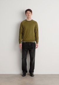 Olijf groene sweatshirt met raglanmouwen, ronde hals en geribde zoom, gecombineerd met donkere denim jeans en zwarte schoenen. Eenvoudige, moderne pasvorm.