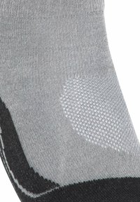 Grå strumpa med svarta häl- och tåsektioner, med en texturerad vit halkskyddsfläck på sulan.