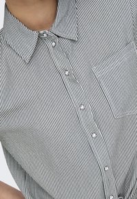 Camicia a maniche corte a righe bianche e nere, con colletto a punta, taschino sul petto e texture in cotone liscia.