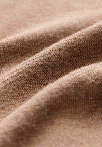 Struktureret stof i blød beige tone, der viser fine strikkemønstre og bløde folder, hvilket fremhæver den glatte, hyggelige tekstur.