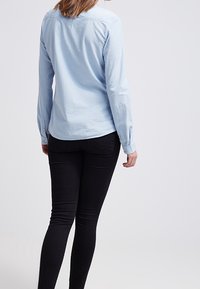 Ljust blå långärmad skjorta med knäppning vid manschetterna och rundad nederkant, matchad med svarta skinny jeans. Slät tygtextur.