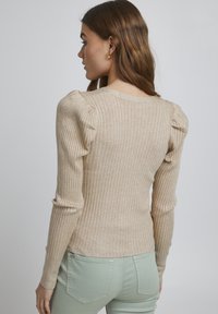 Beige ribbet trøje med lange ærmer, der har puffede skuldre og en tætsiddende silhuet, tilsat lysegrønne bukser.