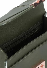 Bolso de mano de cuero sintético verde oliva con un interior que incluye un compartimento con cremallera, bolsillos planos y un acento de hardware en color rosa dorado brillante.