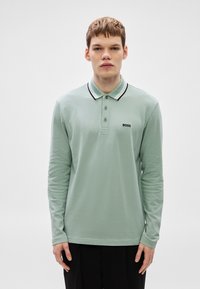 Polo de manga comprida em algodão verde claro, com gola canelada preta e branca, pala com três botões e logótipo "BOSS" preto no peito.