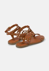 Brązowe sandały na paski z gładkiej skóry, ozdobione srebrnymi ćwiekami i zapięciem na klamrę, z płaską gumową podeszwą.