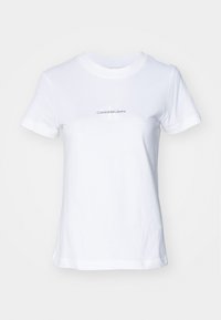 T-shirt in cotone bianco con collo rotondo, maniche corte e grafica frontale con testo blu: "CalvinKleinJeans" con un logo "K" stilizzato.