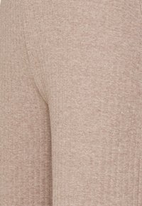 Ribbat, ljusbrunt tyg med en mjuk textur. Designen har en kroppsnära form och synliga sömmar för att ge extra detalj.