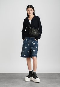 Fekete bordás kardigán egy fehér ing felett, kék virágmintás hímzett farmer rövidnadrággal és fekete platform tornacipővel párosítva. Fekete kézitáska felirattal.