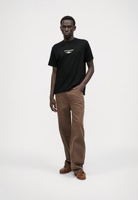 T-shirt de algodão preta com pequeno logotipo branco, combinada com calças largas de veludo cotelê castanho e sapatos castanhos. Design minimalista, textura suave.