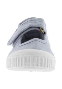 Scarpa di tela azzurro chiaro con suola in gomma bianca testurizzata e cinturino regolabile con chiusura a velcro vista frontalmente.