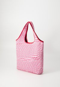 Rdeča torba iz blaga z ponavljajočim se belim logotipom, narejena iz trpežnega materiala, z širokimi, zaobljenimi ročaji in prostornim notranjostjo.