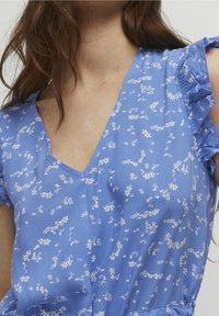 Blå blommig klänning i lätt tyg med volangärm, V-ringning och subtila vita blommönster genomgående.