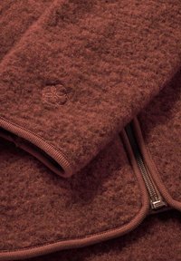 Brauner, gefilzter Wollkleidungsstück mit einer glatten Textur, das über einen Reißverschluss und ein gesticktes Logodetail verfügt. Die Kanten sind mit einem kontrastierenden Finish eingefasst.