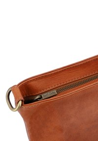 Bruine leren pouch met een ritsluiting, voorzien van een metalen ring en een subtiele textuur. Stikseldetails langs de rand, gelabeld "Gusti Leder."