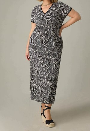 Vrouw draagt een zwart-witte midi-jurk met bladmotief, korte mouwen en zwarte espadrille sleehakken.