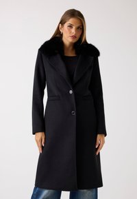 Sort uldfrakke med en faux fur-krave, der har en skræddersyet design, lange ærmer og to knapper. Glat tekstur og klassisk snit.