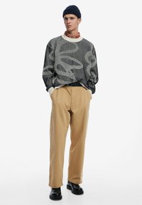 Svart och vit randig tröja med rund halsringning, beige chinos och svarta stövlar. Accessoarer inkluderar en röd bandana och en marinblå mössa.