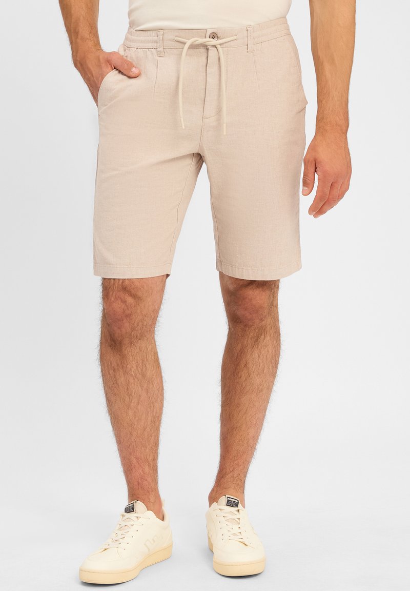 Light beige shorts made of textured fabric, featuring an elastic waistband with drawstrings and side pockets. Worn with white sneakers.