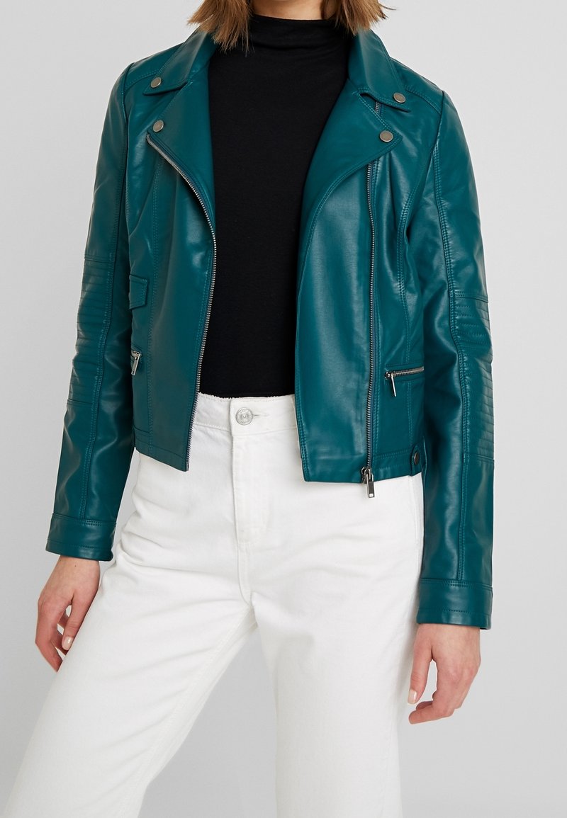 Tealowa ramoneska z ekoskóry o krótkim fasonie, z zapięciem na zamek, zatrzaskami i podszytymi ramionami. Nosi się ją na czarnej bluzce.