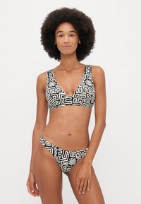 Czarny i biały bikini w wzory z topem w kształcie V, szerokimi ramiączkami i niskim stanem, wykonane z elastycznego materiału z geometrycznymi wzorami.