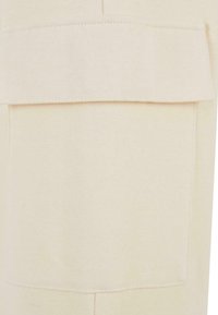 Tissu de sweat-shirt beige avec une grande poche avant aplatie. La texture est douce avec des accents de couture visibles, créant un design minimaliste.