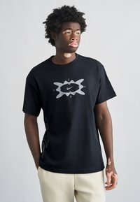 Μαύρο βαμβακερό T-shirt με μεγάλο γκρι γραφικό λογότυπο μπροστά και διακοσμητικό σχέδιο στο πλάι. Στρογγυλή λαιμόκοψη και κοντά μανίκια.