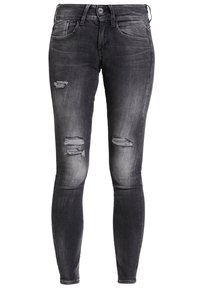 Chude dżinsy w wyblakłym czarnym deninie, z przetarciami i dużymi dziurami z przodu. Klasyczny pięciokieszeniowy fason z zapięciem na zamek.