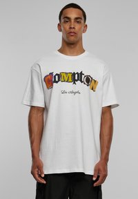 Bijela pamučna majica s opuštenim krojem, s raznobojnom grafikom "Compton, Los Angeles" u različitim fontovima i stilovima na prednjem dijelu.