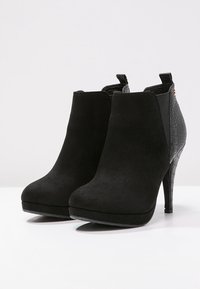 Botas de tobillo de ante negro con un tacón alto y estrechado, un acento de cuero texturizado en la parte posterior y un diseño de punta redonda.