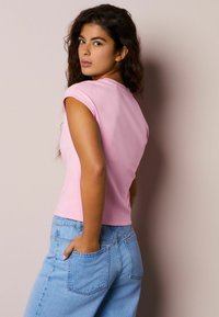 Roza oprijet vrh s kratkimi rokavi, združen s svetlo modrimi kavbojkami. Vrh ima okrogel izrez in gladko teksturo.