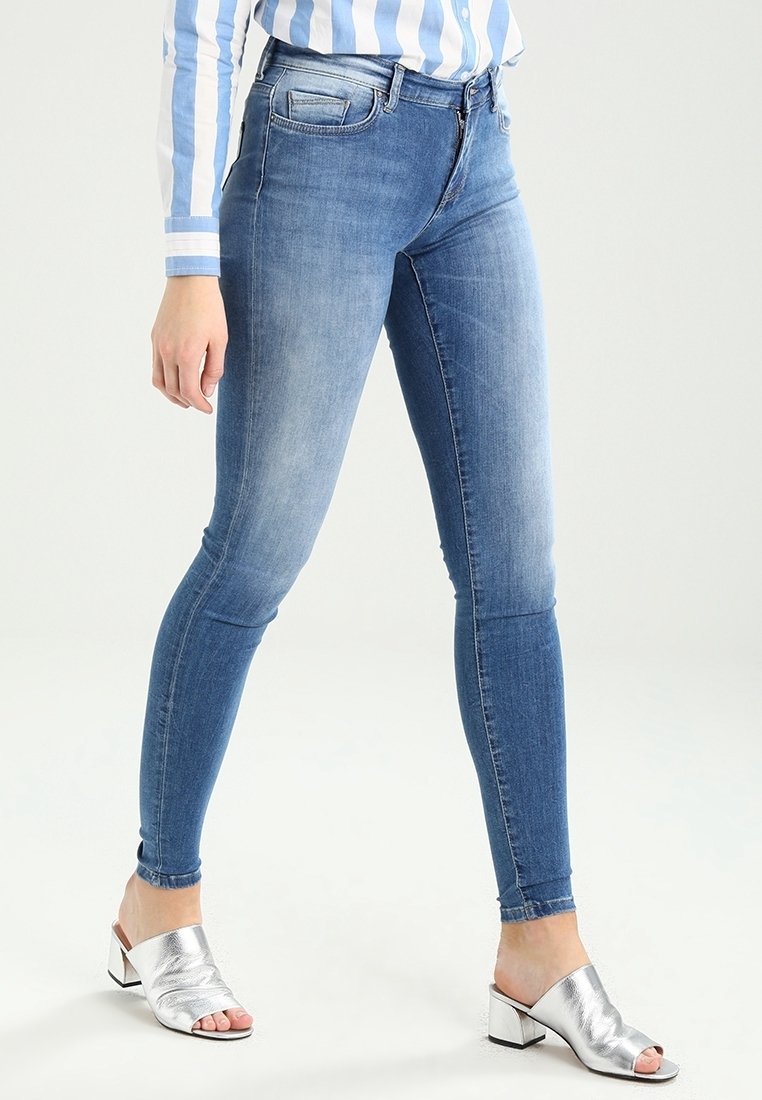Blå denimskinnyjeans med tvättad look, fem fickor och midjehöjd. Matchas med silverfärgade klacksandaler med öppen tå.