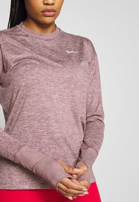Maglia a maniche lunghe Nike in colore rosa mélange, con scollo arrotondato, polsini con foro per il pollice e piccolo logo sul petto a sinistra.
